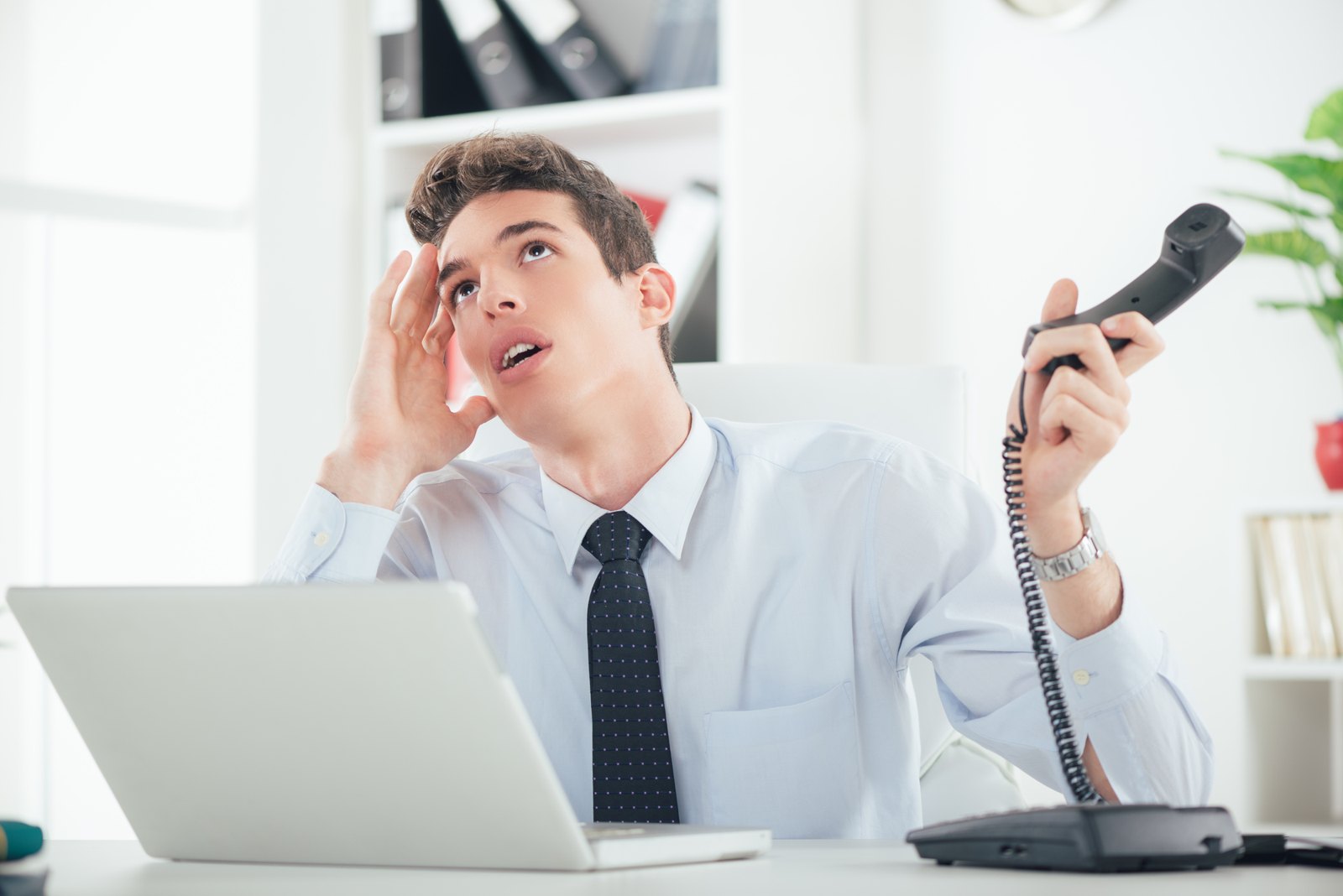 Office worker holding a telephone beside a laptop
